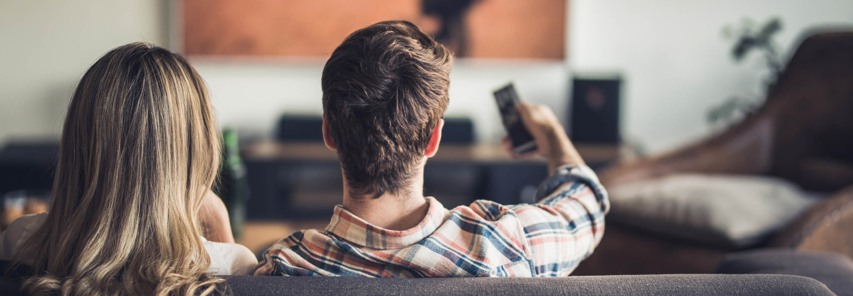 Vi ser bakhodene til to mennesker som sitter i en sofa og ser på TV